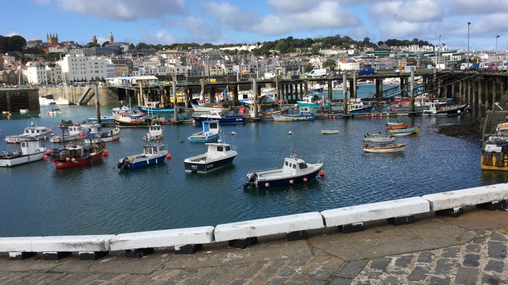 Lots of boats moored in Guernsey harbour, with a few vans crossing a bridge amongst them.
