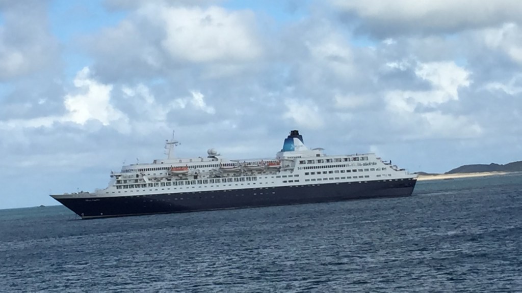 Close-up of a large ferry near Guernsey harbour, with white buildings on he deck above a blue underside.