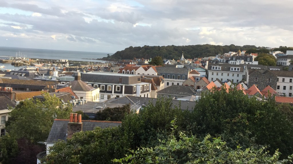 View from La Fregate Hotel in Guernsey over lots of rooftops towards the sea and tall cliffs in the distance.