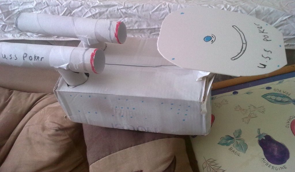Side view of a white cardboard model of the Starship Enterprise, named the USS Poker, with 2 thrusters on the back and the big circular deck sticking out over the front.