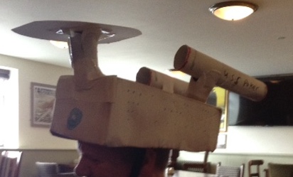 Side view of Glen's friend wearing the white cardboard Starship Enterprise model as a hat.
