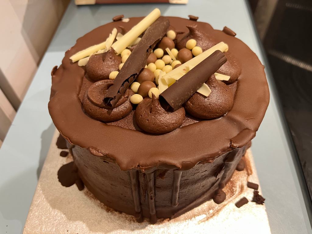 A Sainsbury's Taste The Difference Loaded Chocolate Cake. This is a big round chocolate sponge cake layered with rich chocolate buttercream, and with a mixture of white chocolate and milk chocolate decorations on the top.