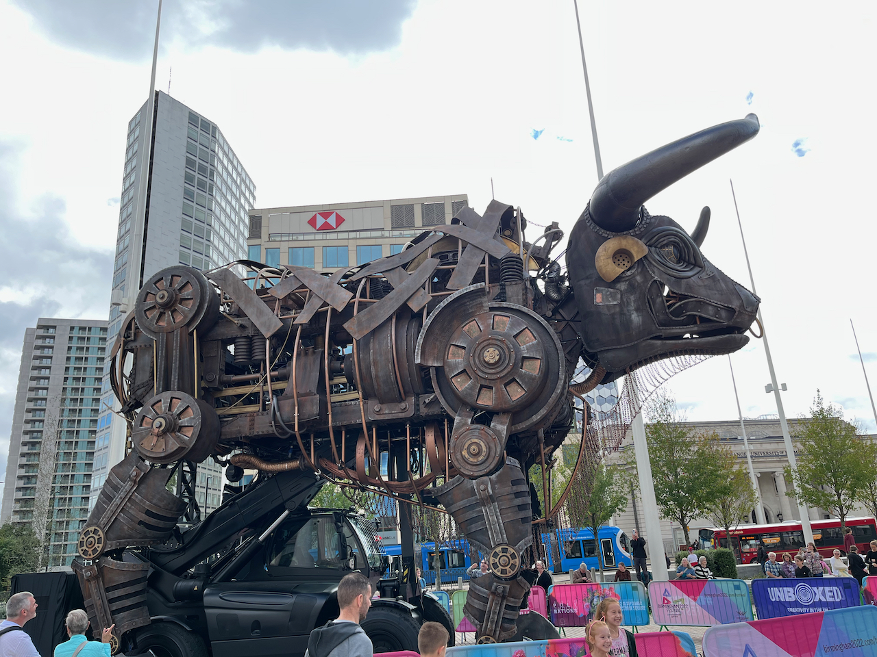 Right side view of the huge animatronic bull from the Commonwealth Games, with people standing near the surrounding barrier to take photos of it.