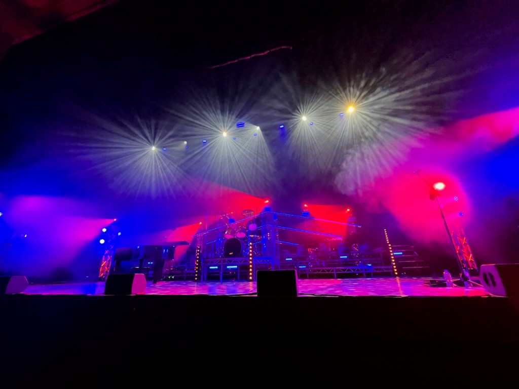 The stage for the Queen Machine Symphonic concert, including a piano, drum kit and seating for the backing orchestra.