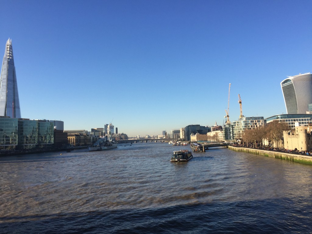 View along the Thames from Tower Bridge towards London Bridge, with the Shard on the left and the Walkie Talkie building on the right, on a sunny day beneath a clear blue sky.