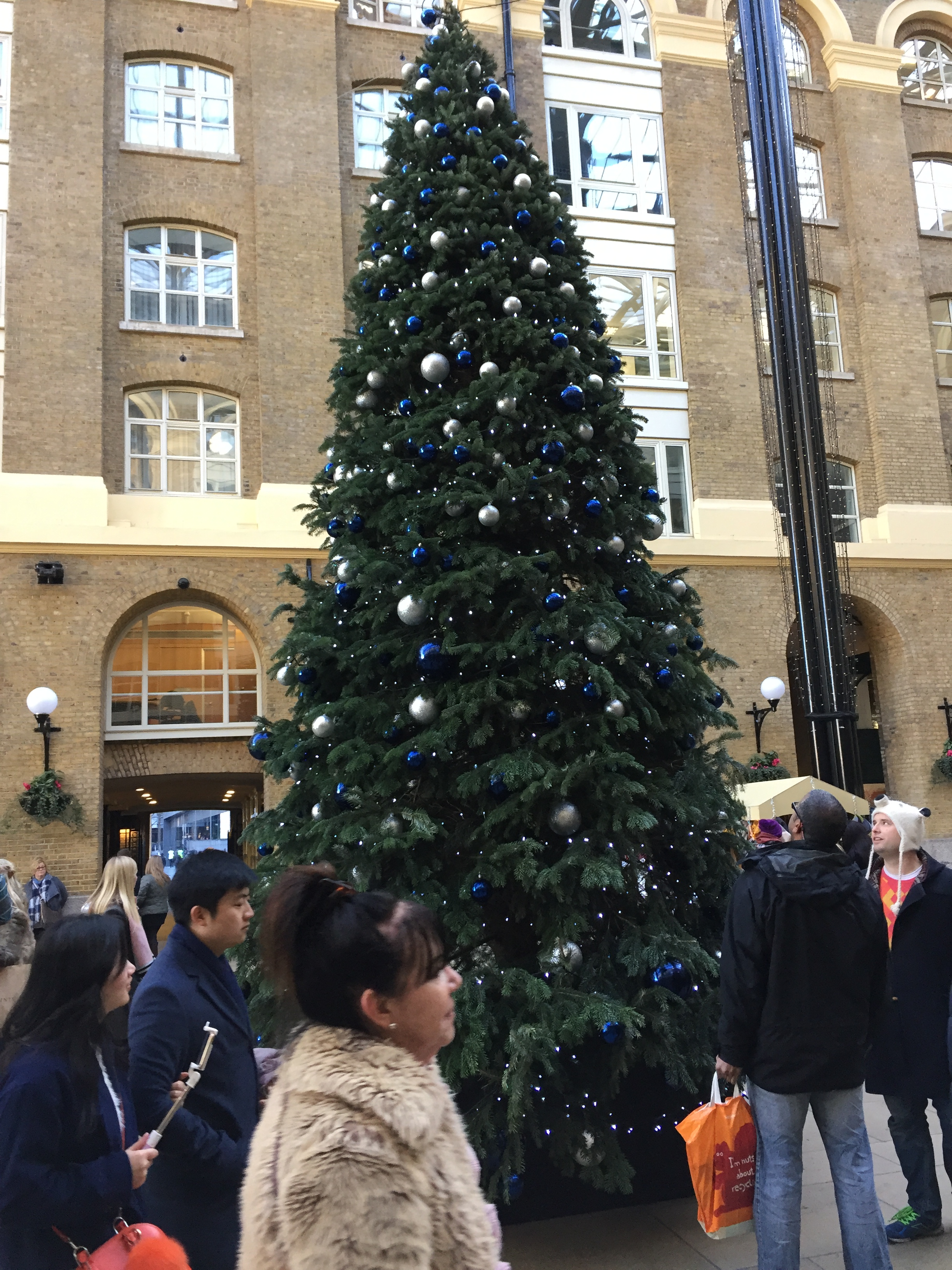 A tall green Christmas tree, decorated with lots of blue and silver baubles and strings of lights, in Hay's Galleria in London.