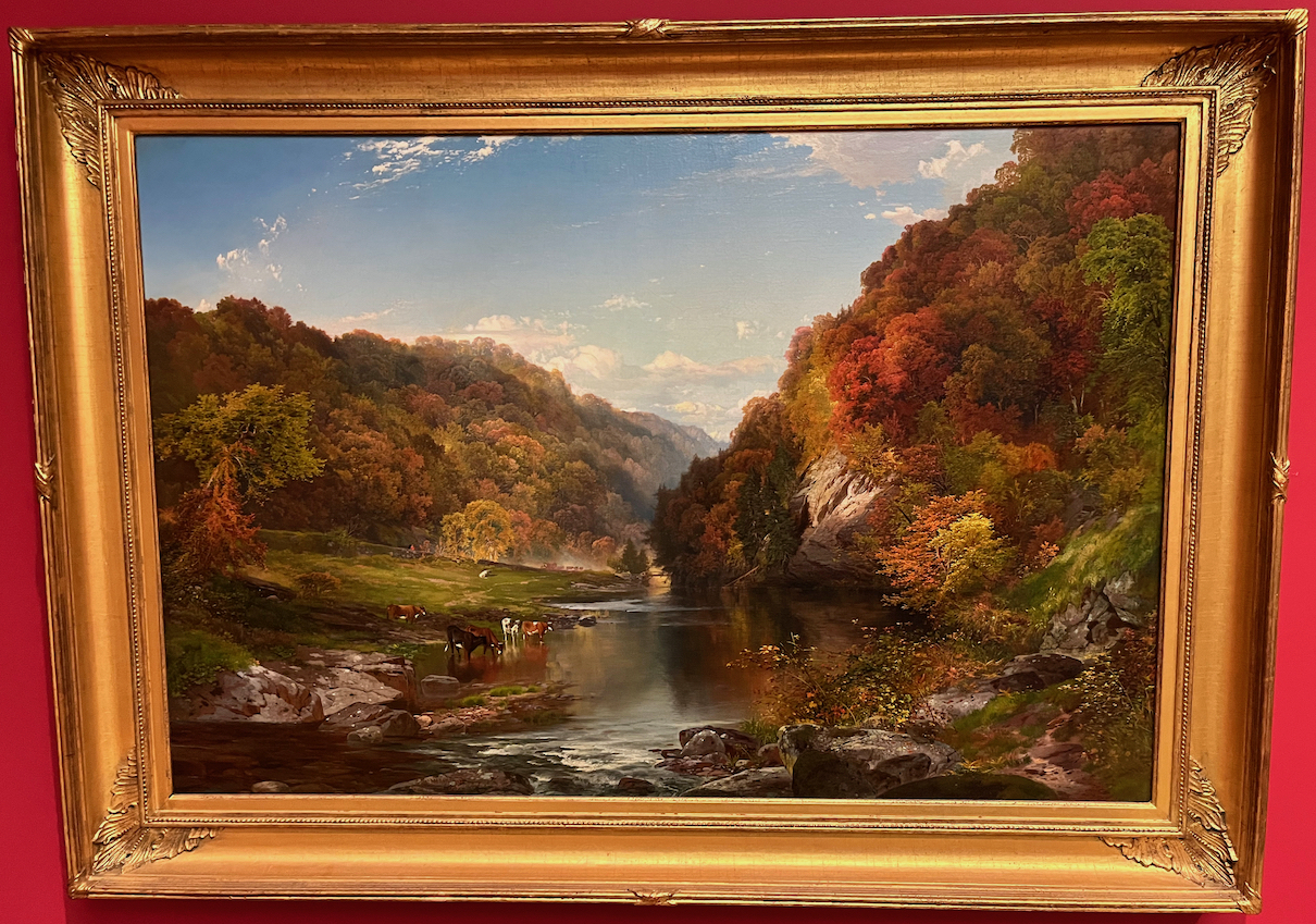 A scenic painting of a river surrounded by tall hills covered in trees, with a few cows standing and drinking in the shallow water by the bank.