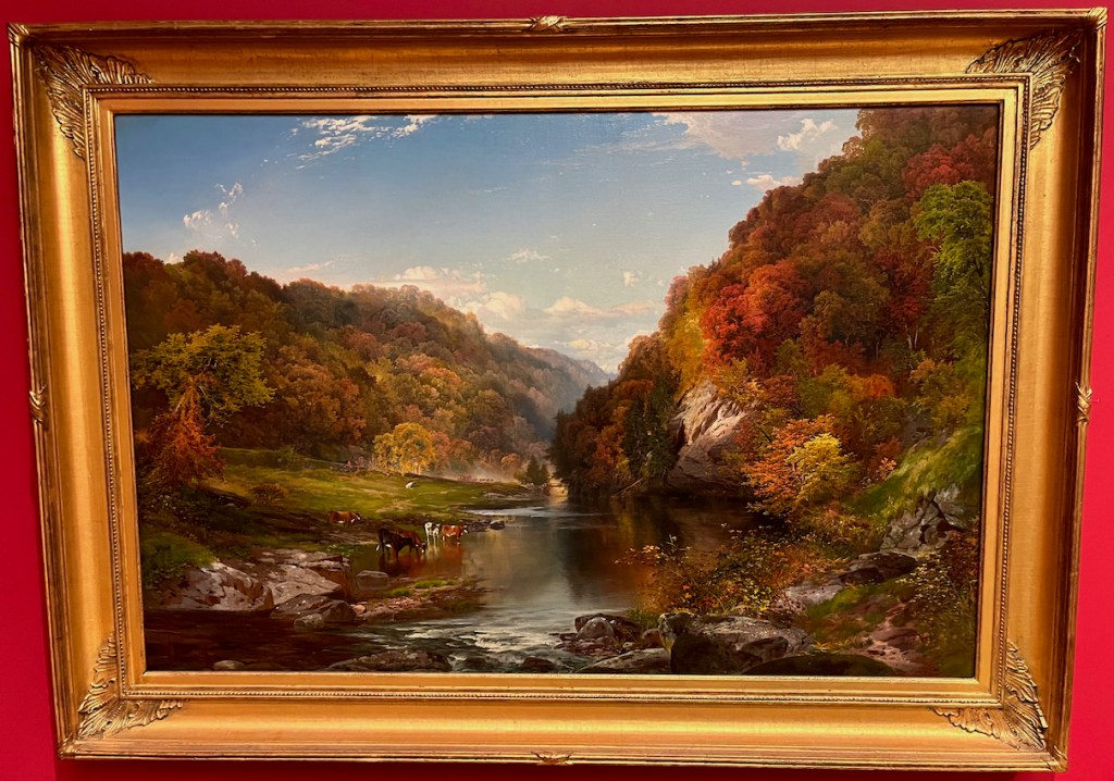 A scenic painting of a river surrounded by tall hills covered in trees, with a few cows standing and drinking in the shallow water by the bank.