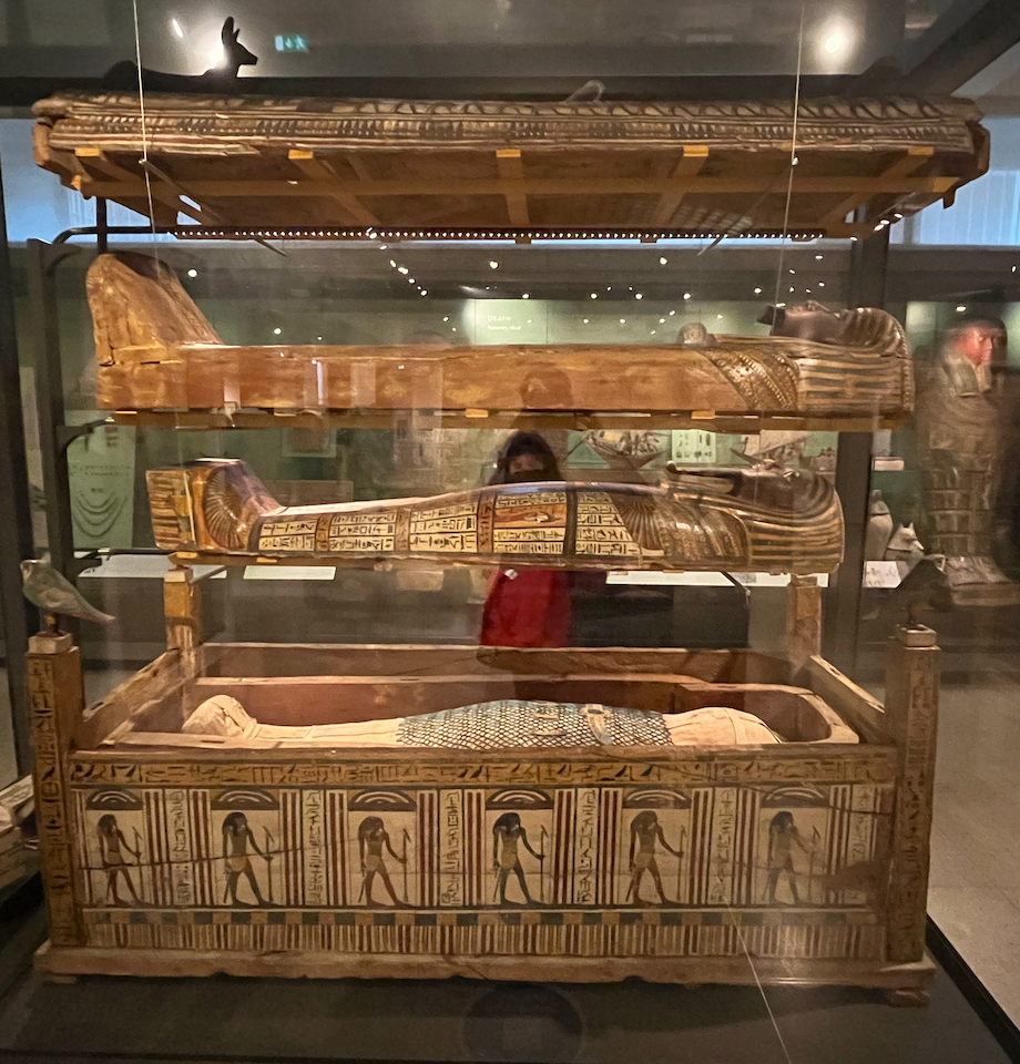 A tall nest of 3 coffins, one above the other, with the bottom one open to reveal a mummified figure.