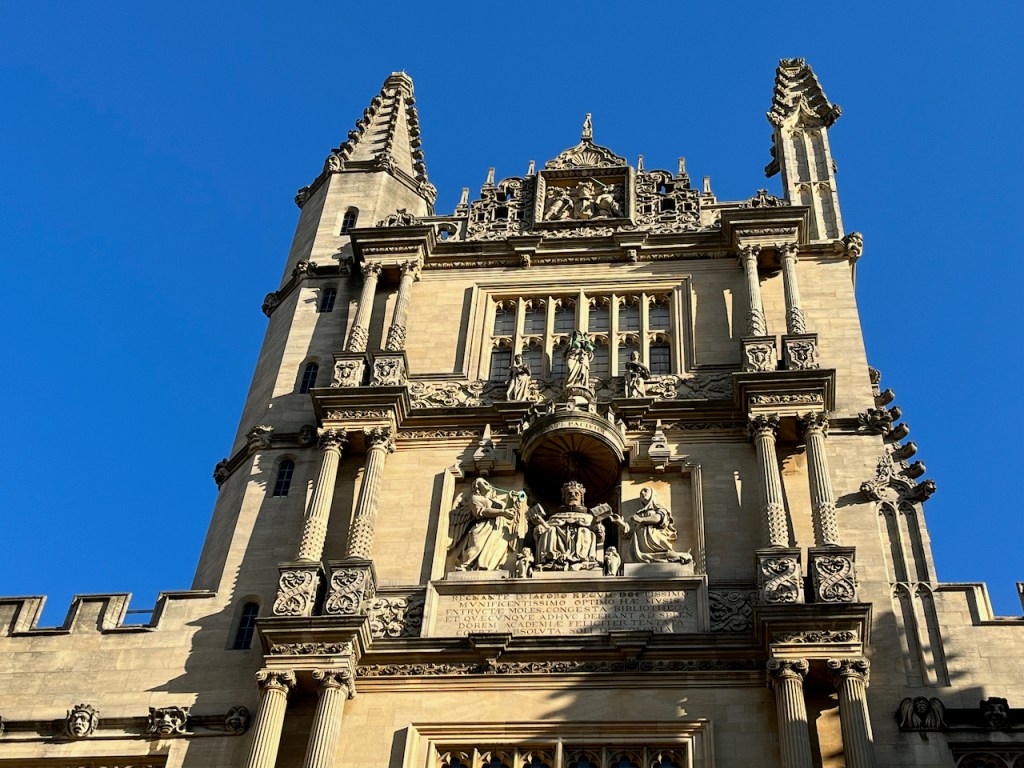 Close-up of the statues, Latin text and other engraved patterns on the tower above the entrance to the Bodleian Library quadrangle.