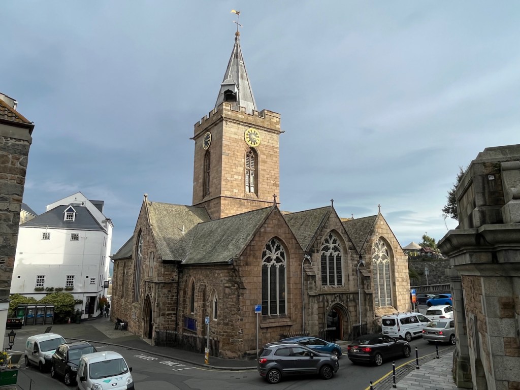 The large town church in St Peter Port, Guernsey, with a spire on top of a square tower in the centre of the building.