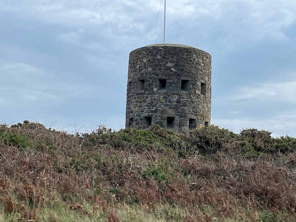 A circular stone tower, with 2 rows of small square windows all around it, in a large grassy area.