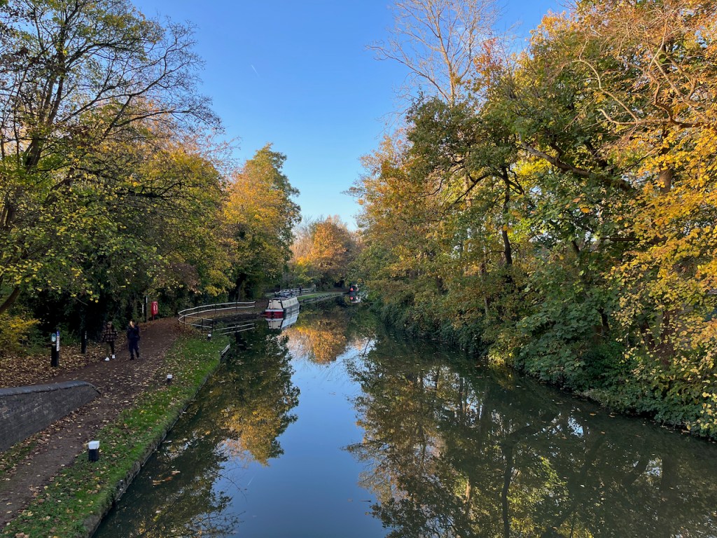 View along the Oxford Canal, with trees on either side and narrowboats in the distance, beneath a clear blue sky.