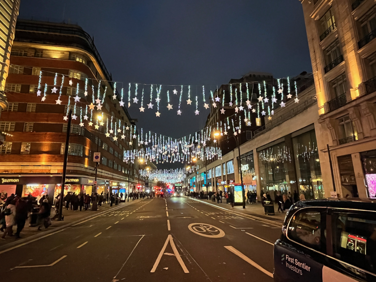 Bright stars dangling on illuminated threads of varying lengths, hanging from thin cables over Oxford Street, either straight across the road, or at diagonals so that cables overlap with each other.