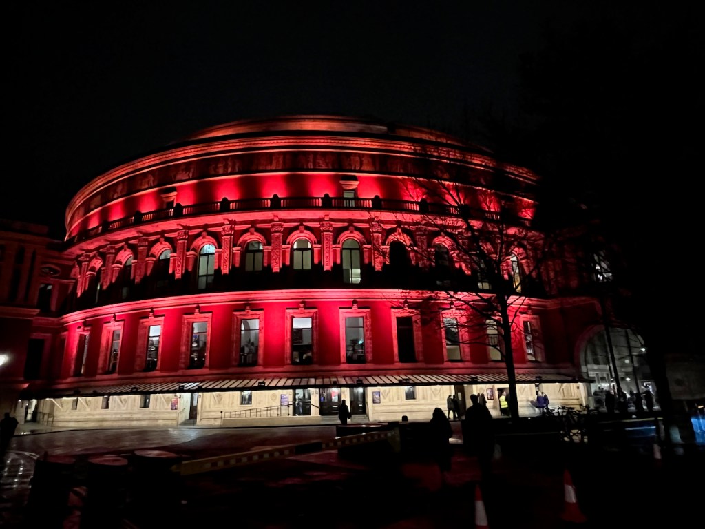 The huge circular Royal Albert Hall building lit up in red.