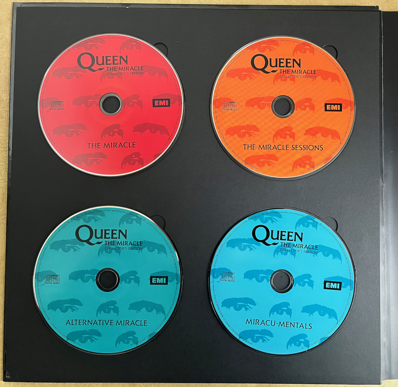 The 4 music CDs from Queen's box set for The Miracle, which are coloured red for the main album, orange for the sessions, turquoise for the alternative tracks and light blue for the instrumentals.