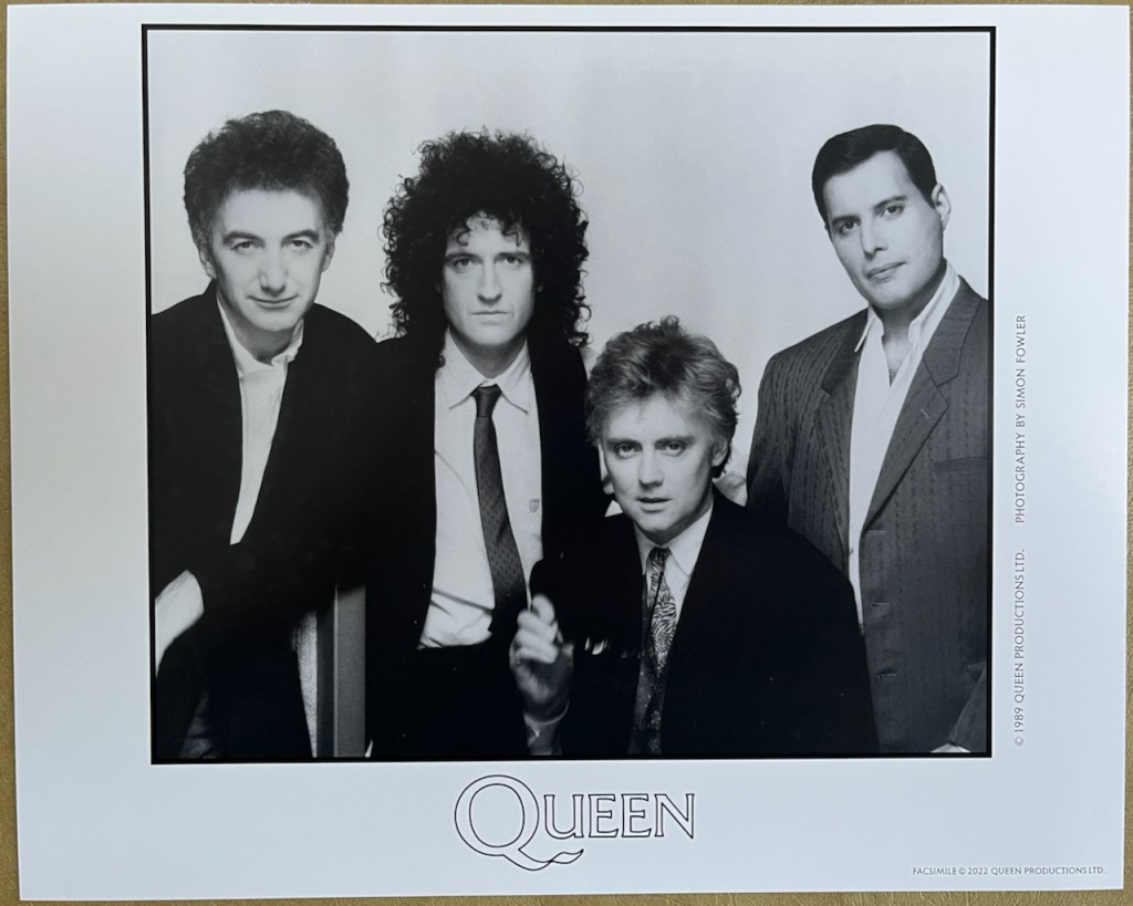 A glossy black and white photo of Queen, from left to right showing John, Brian, Roger and Freddie.
