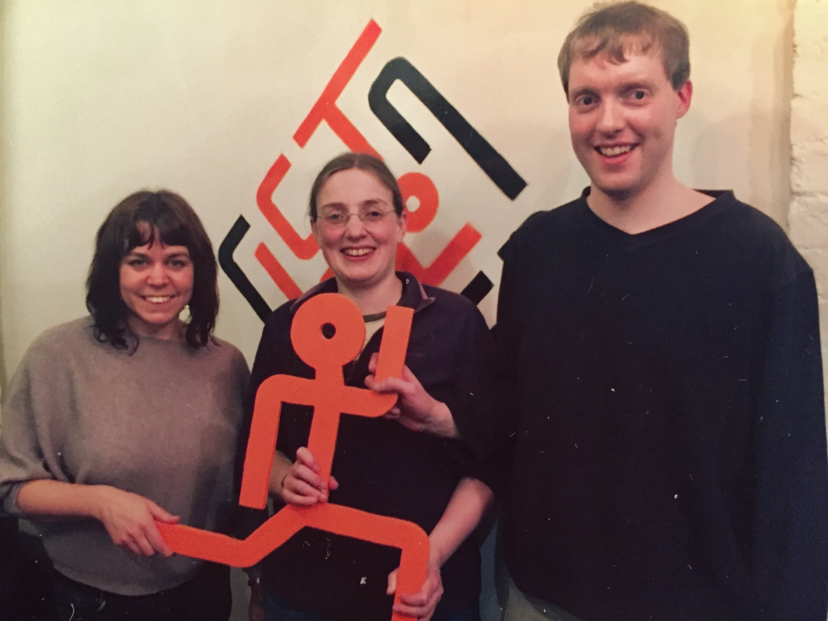 Glen with 2 ladies posing for a photo after completing the ClueTrace escape room. Between them they're holding a big orange running stick man figure.