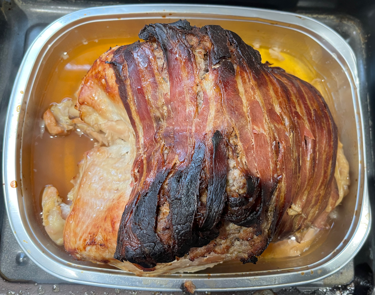 Cooked M&S turkey crown with bacon on top in a foil tray.