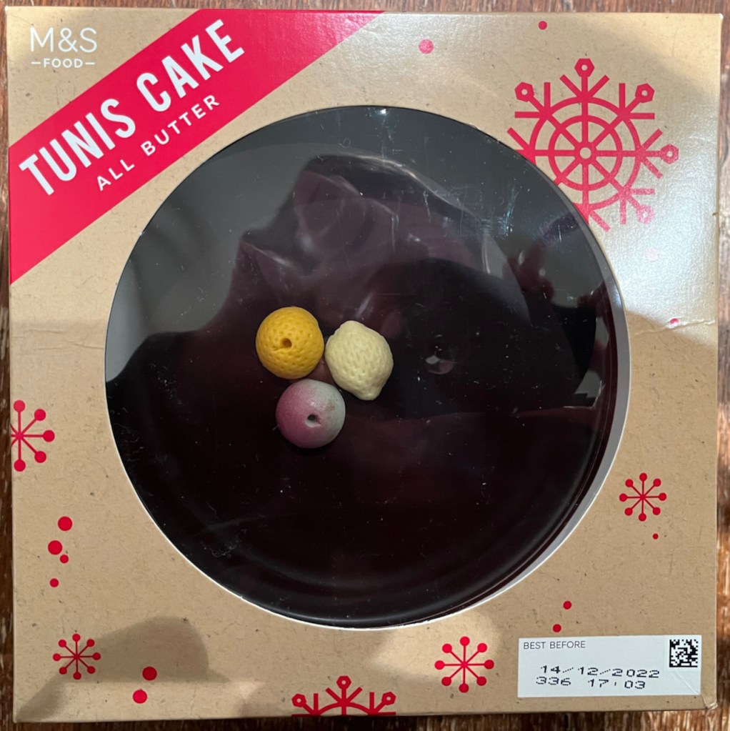 M&S Tunis Cake, a round sponge cake with a thick layer of chocolate on top decorated with 3 little marzipan fruits.