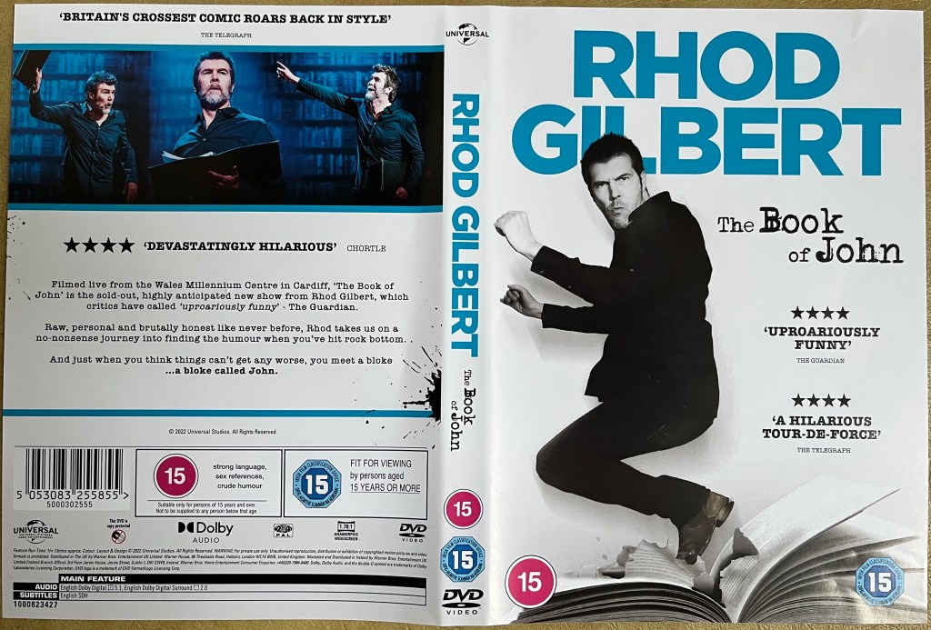 DVD cover spread for Rhod Gilbert - The Book Of John. The front cover shows Rhod standing on the open pages of a large book, while the back cover has images from the show above the description of the DVD.