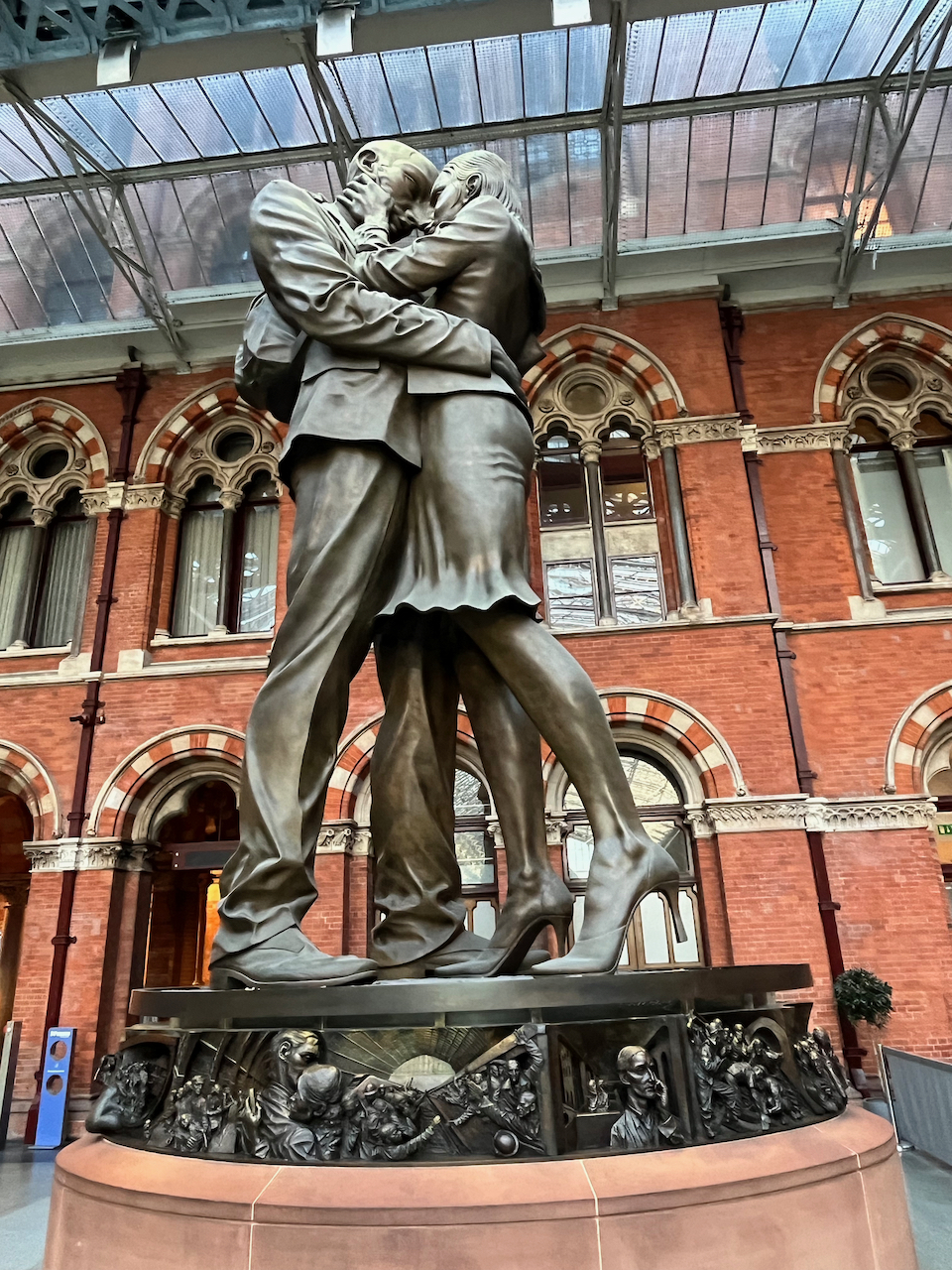 The Meeting Place by Paul Day is a 9 metre (30 foot) high sculpture depicting a man and a woman embracing, with his right hand around her waist and her left hand caressing his cheek, as they look into each other's eyes romantically. A bronze relief all around the plinth below them includes very detailed sculptures of commuters on the station concourse or in train carriages, from a woman with a dog to big crowds of people all crammed together, plus engineers working on the tracks.
