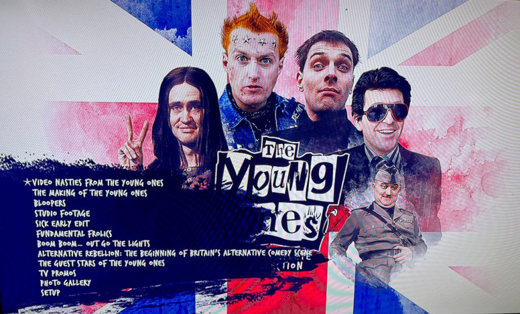 The menu on the bonus Blu-ray disc in the box set for The Young Ones. The main characters and the show's logo are shown in front of a Union Jack, and a long menu of options is overlaid in the bottom left corner, in white text on a dark blue background.