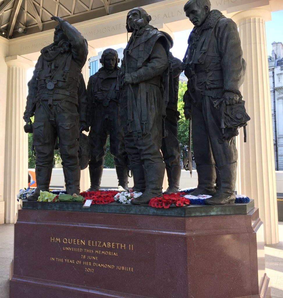 The Bomber Command Memorial in Hyde Park, featuring statues of 4 squadron members. Gold lettering on the plinth they're standing on reads HM Queen Elizabeth II unveiled this memorial 28 June in the year of her Diamond Jubilee 2012.