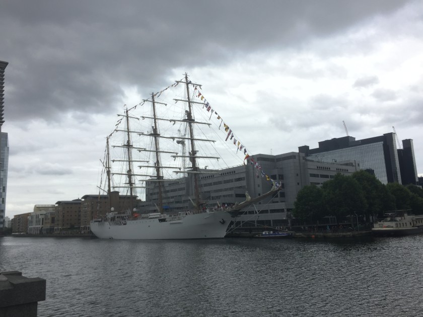 A large ship with 3 very tall masts in the South Dock at Canary Wharf.