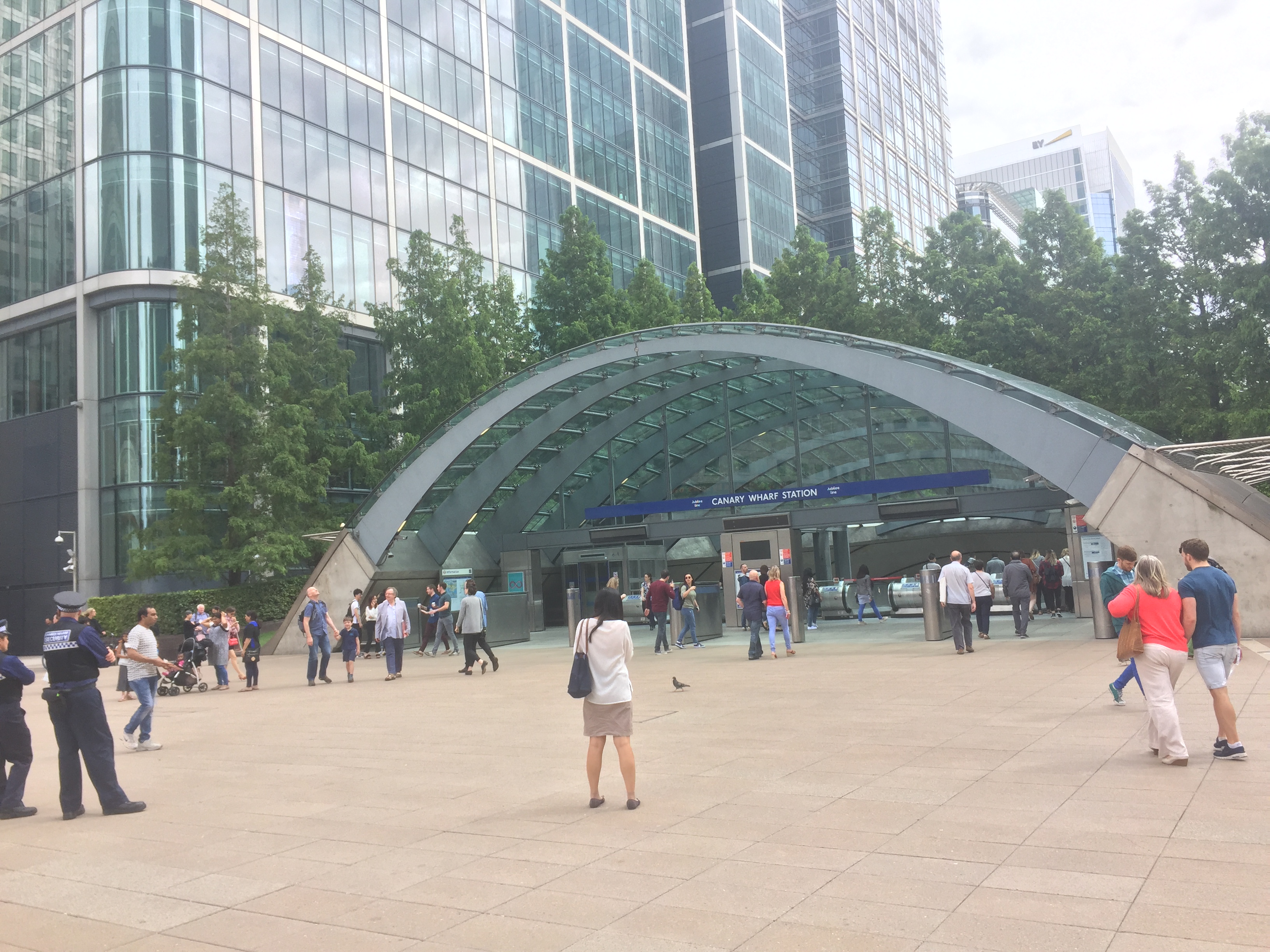 A wide archway over the entrance to Canary Wharf Tube station, with trees behind it.