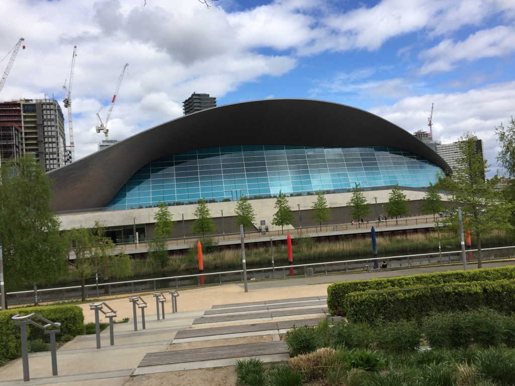 The Aquatic Centre, with its large roof that curves over from one end to the other, and blue glass windows covering the side of the building.