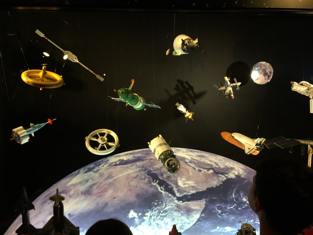 Models of satellites, spacecraft and the moon above an image of planet Earth.