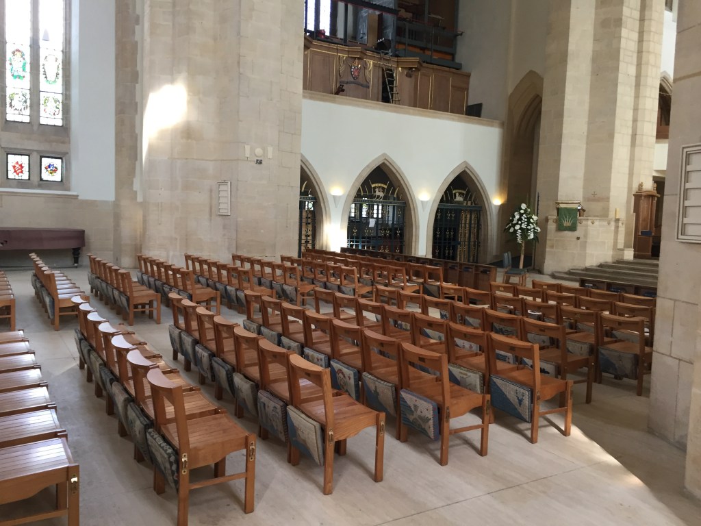 The interior of Guildford Cathedral, including rows of wooden chairs, and archways along the way that each curve to a point in the centre at the top.