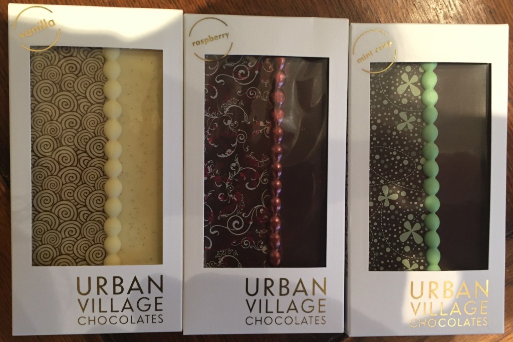 3 bars of chocolate by Urban Village, in vanilla, raspberry and mint crisp flavours. Each bar has a swirly design on the left side, and a plain view of the chocolate on the write, with a line of bobbles down the centre between them.