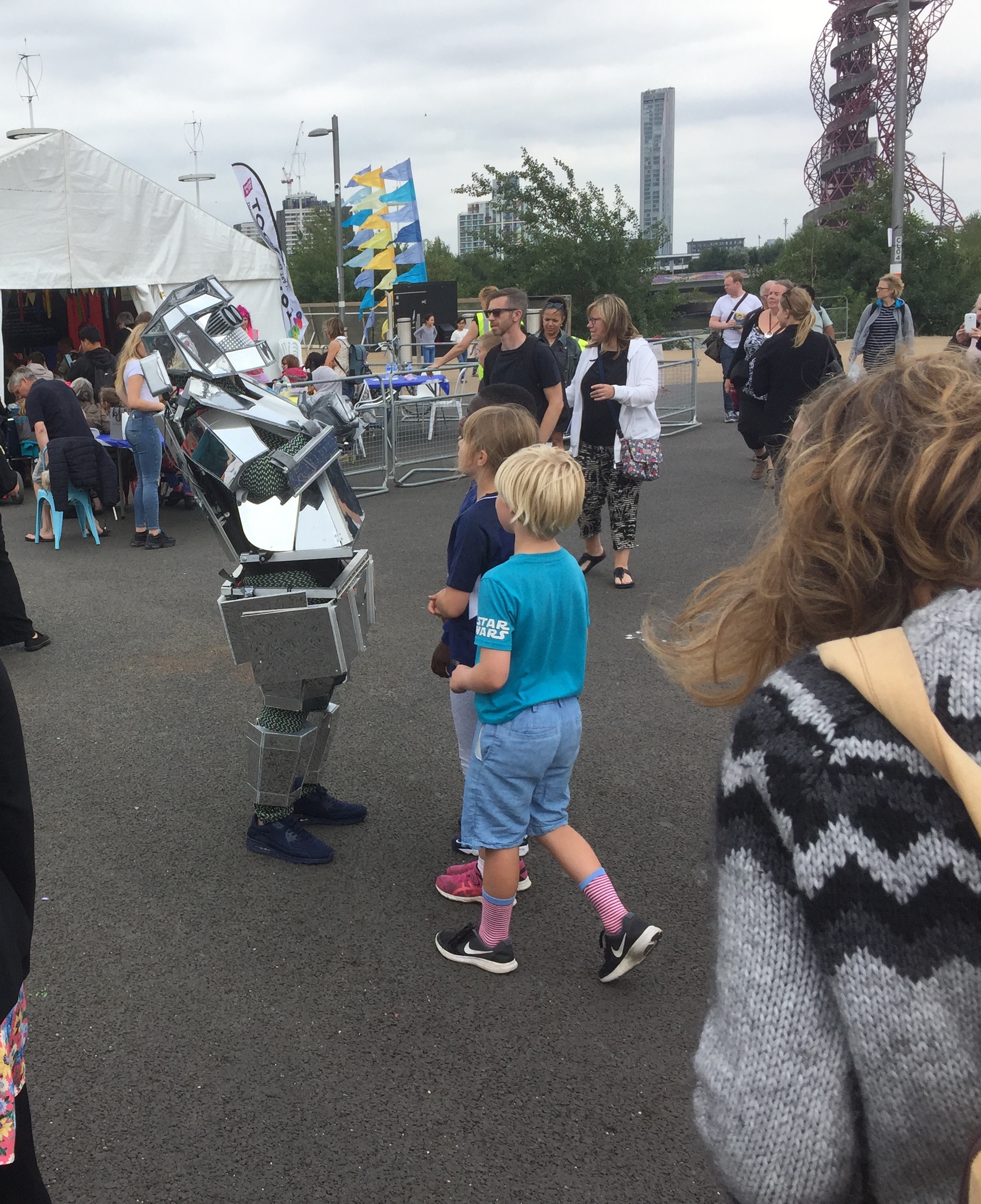 Children watching someone dancing in a metal robot costume in the Olympic Park.