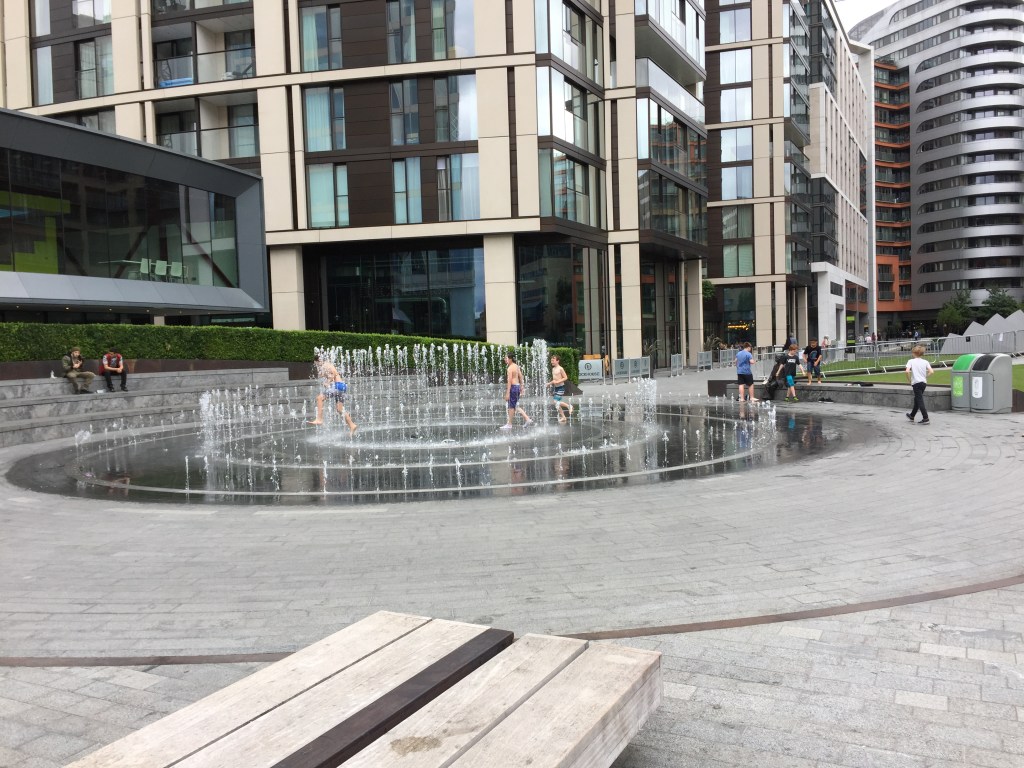 Kids playing in spurting fountains arranged as 3 large concentric circles.