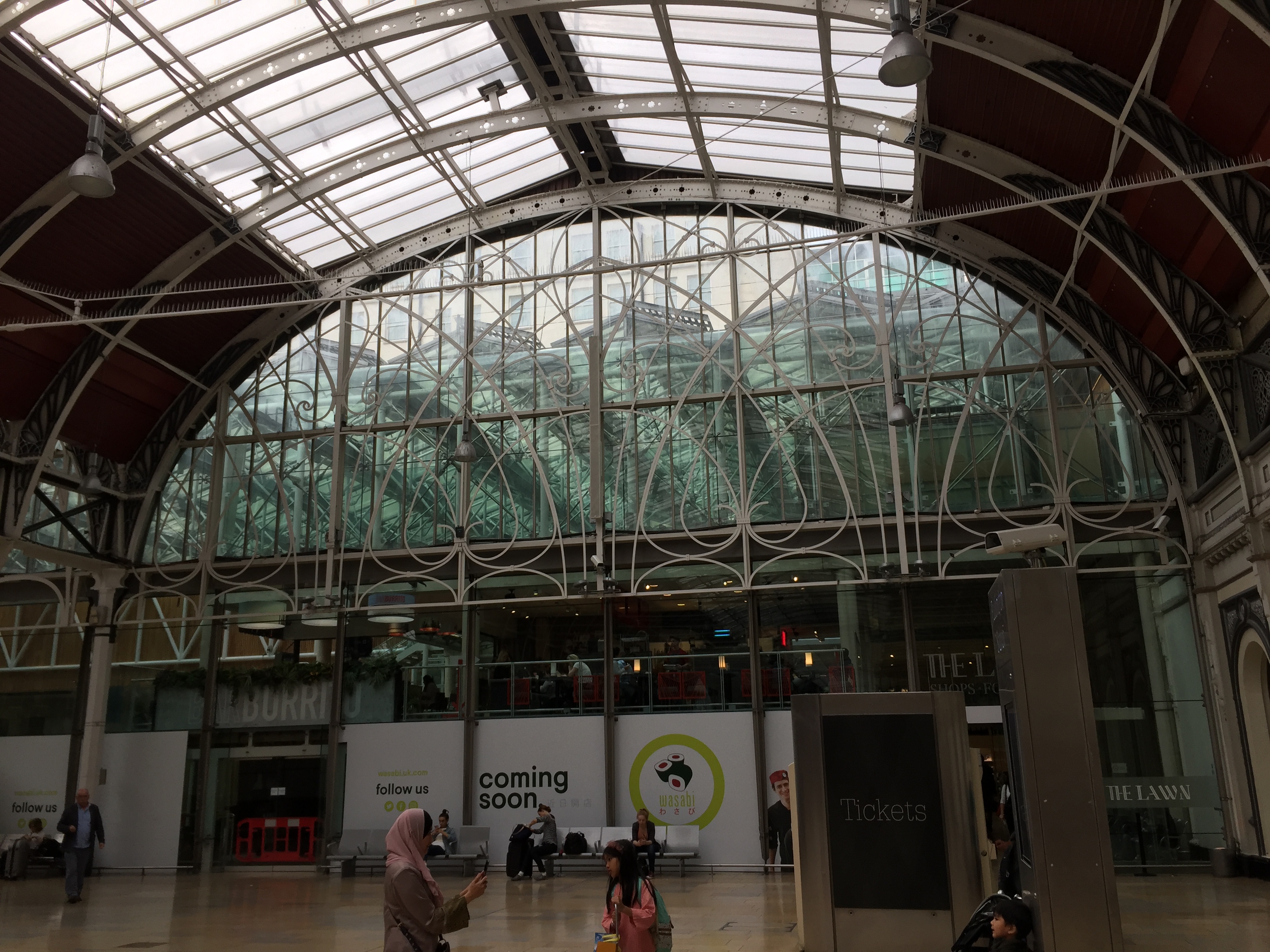 A large arched window with elaborate curved framing across it in Paddington Station.