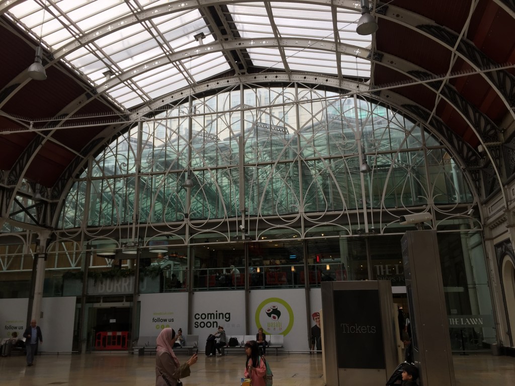 A large arched window with elaborate curved framing across it in Paddington Station.
