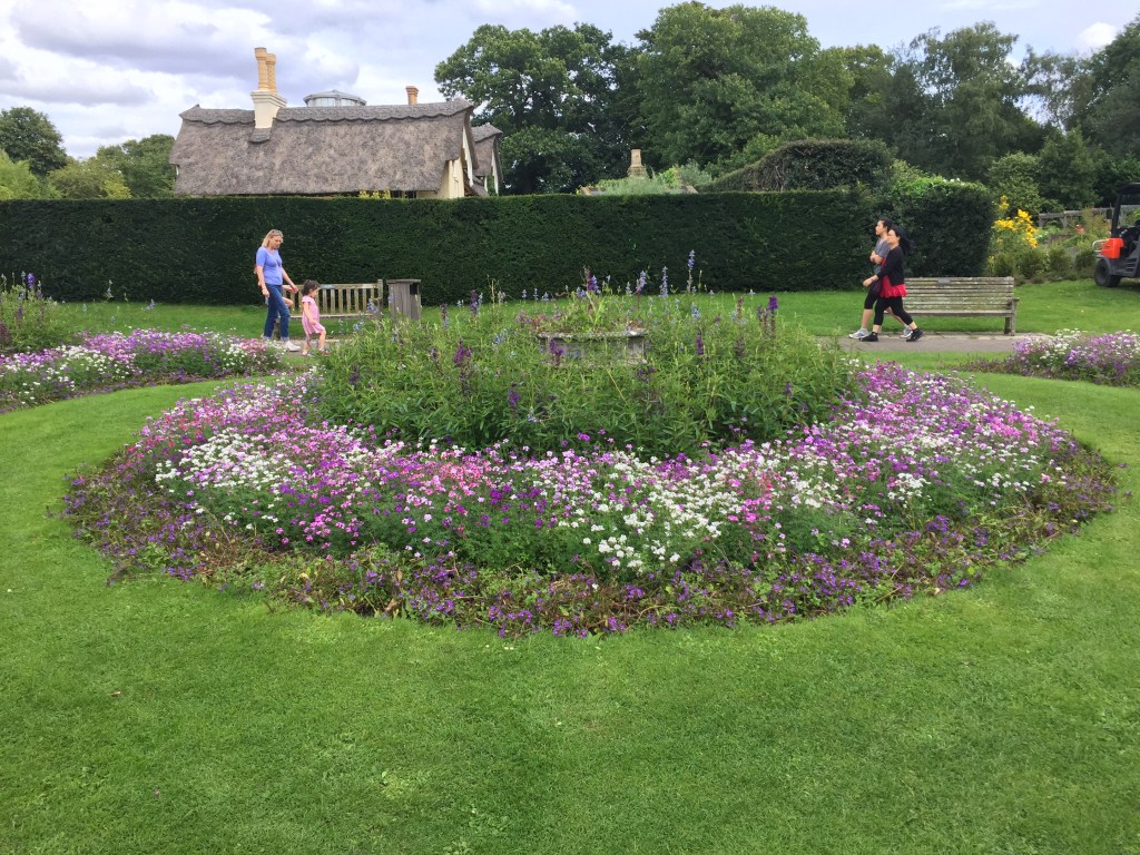 A large round flowerbed with the perimeter full of colourful pink, purple and white flowers, and a few taller colourful flowers in the centre of the circle.