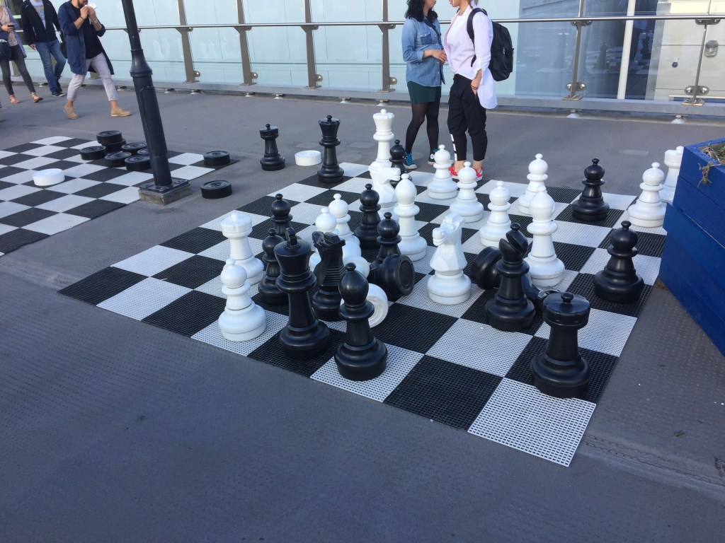 A large chess board with large chess pieces on the pavement on Southend Pier.