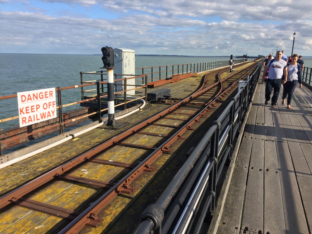 A section of the railway on Southend Pier where the track divides into two. A white sign on a railing has red text that reads Danger, Keep Off Railway.