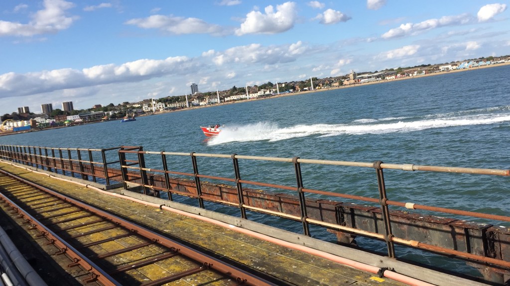 A small fast boat kicking up spray as it zooms past Southend PIer.