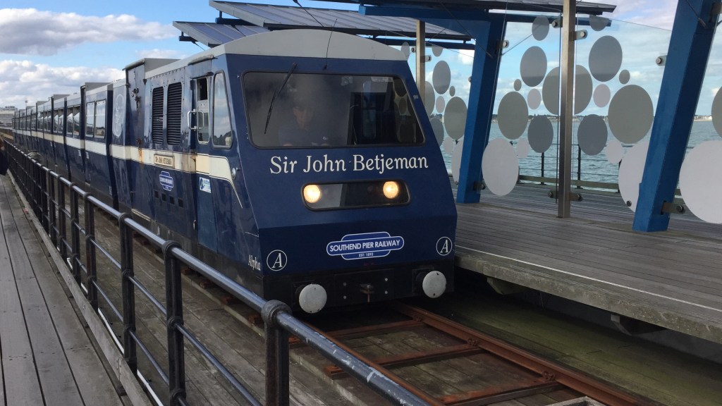 The Southend Pier train, blue in colour with a white stripe along the side and a white roof. White text across the front of the train says Sir John Betjeman.
