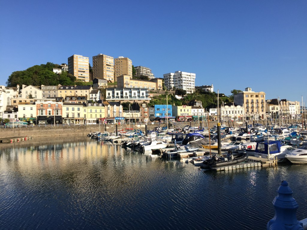 Torquay Harbour in the sunshine, with lots of boats on the water and buildings in the background.