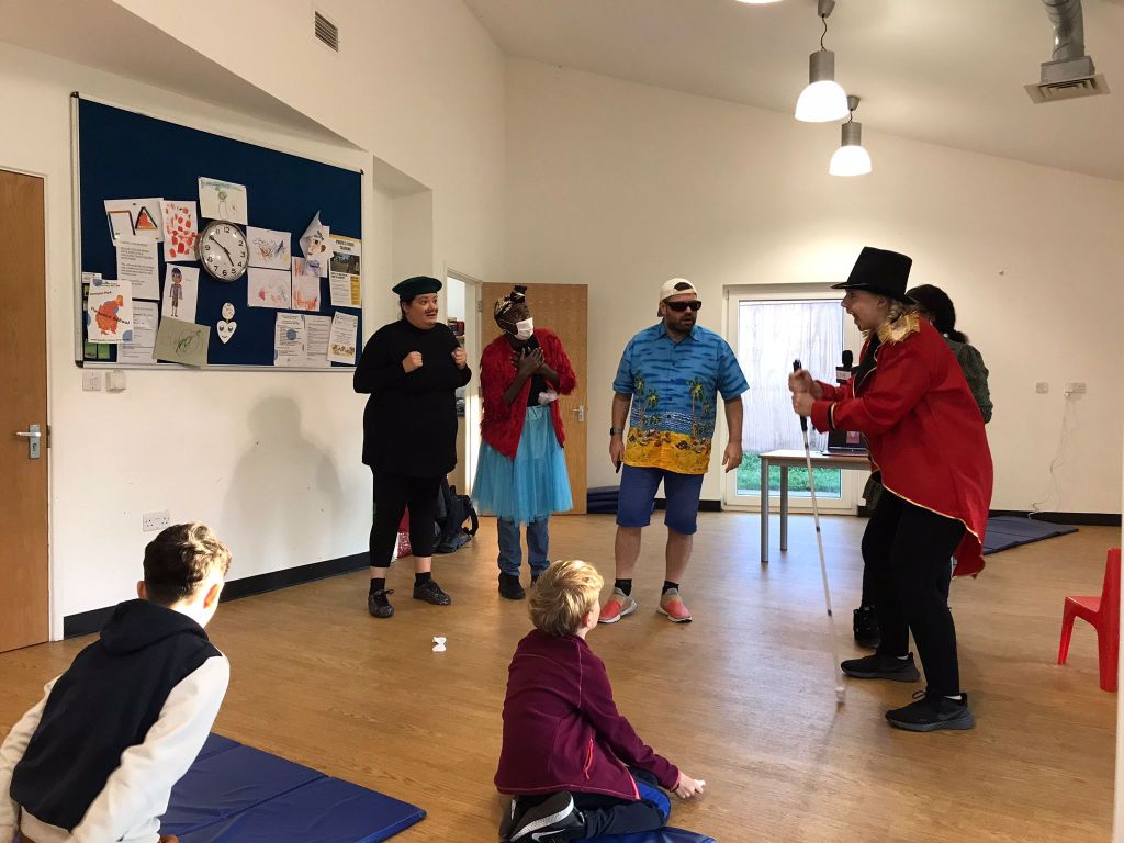 All 5 main cast members of Super Power Panto in the rehearsal studio, one of whom, called Sunblock, is gripping a long cane.
