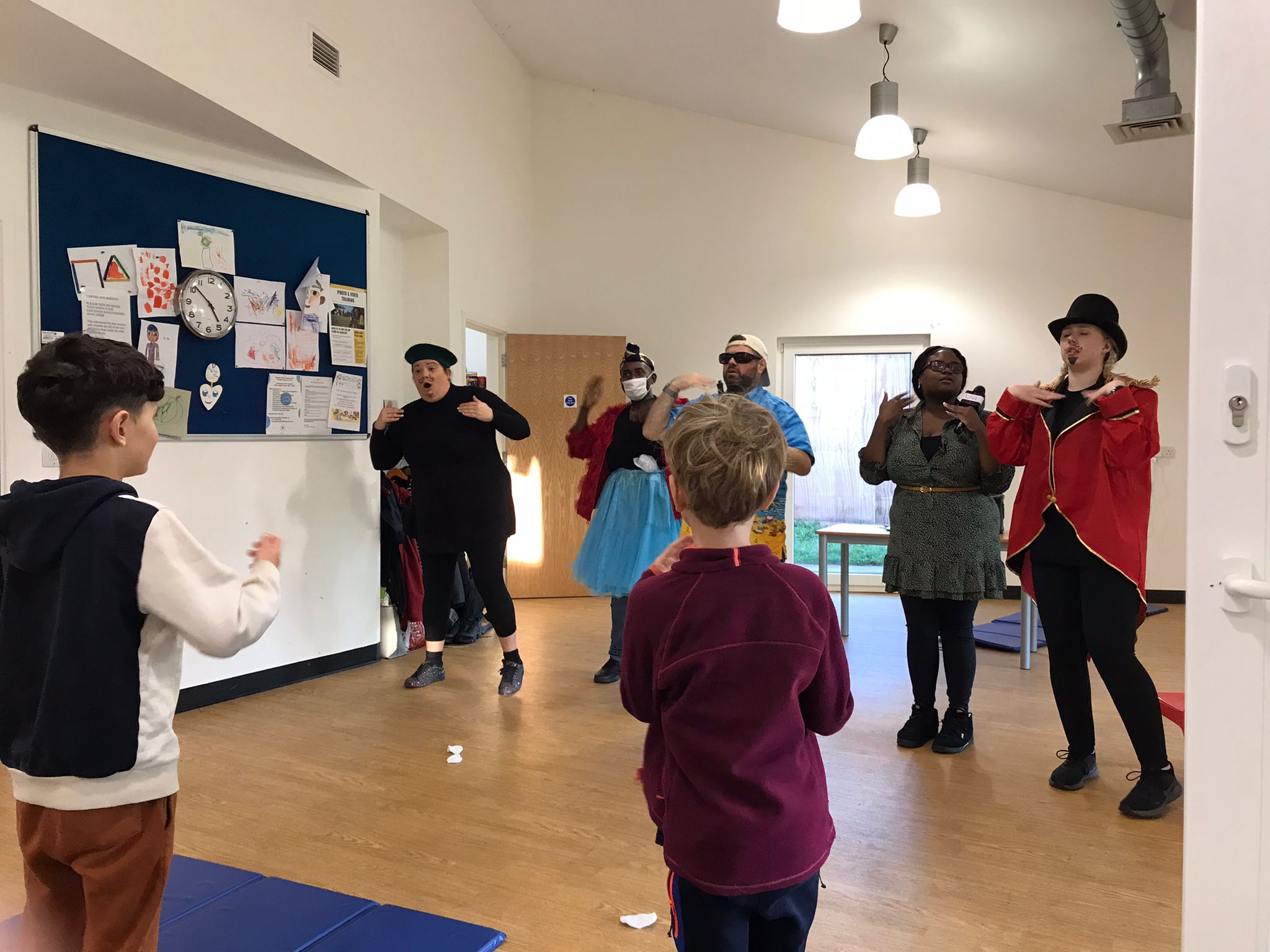 The 5 cast members of Super Power Panto singing and dancing in the rehearsal studio, in front of 2 children who are standing and joining in.