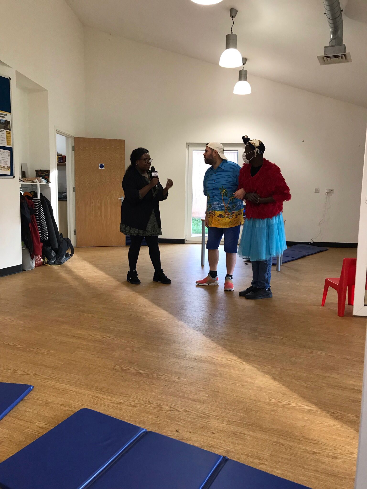 In the Super Power Panto rehearsal room, a female character called Green Grass uses a microphone as she talks to characters called Billy Bright and The Angel of Light.