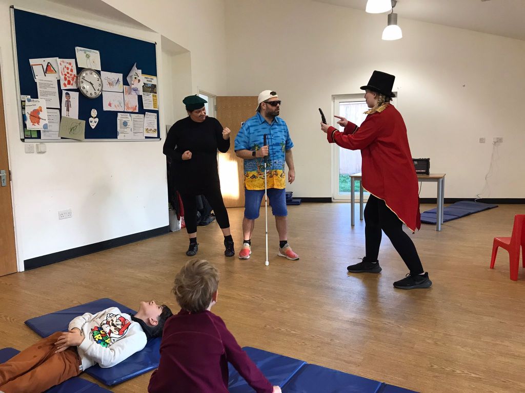 In the Super Power Panto rehearsal studio, Billy and Claude stand together, the latter with his fists held up in a fighting stance, as they look towards Sir Sunblock, who is preparing to press a button on a remote control he's holding up.