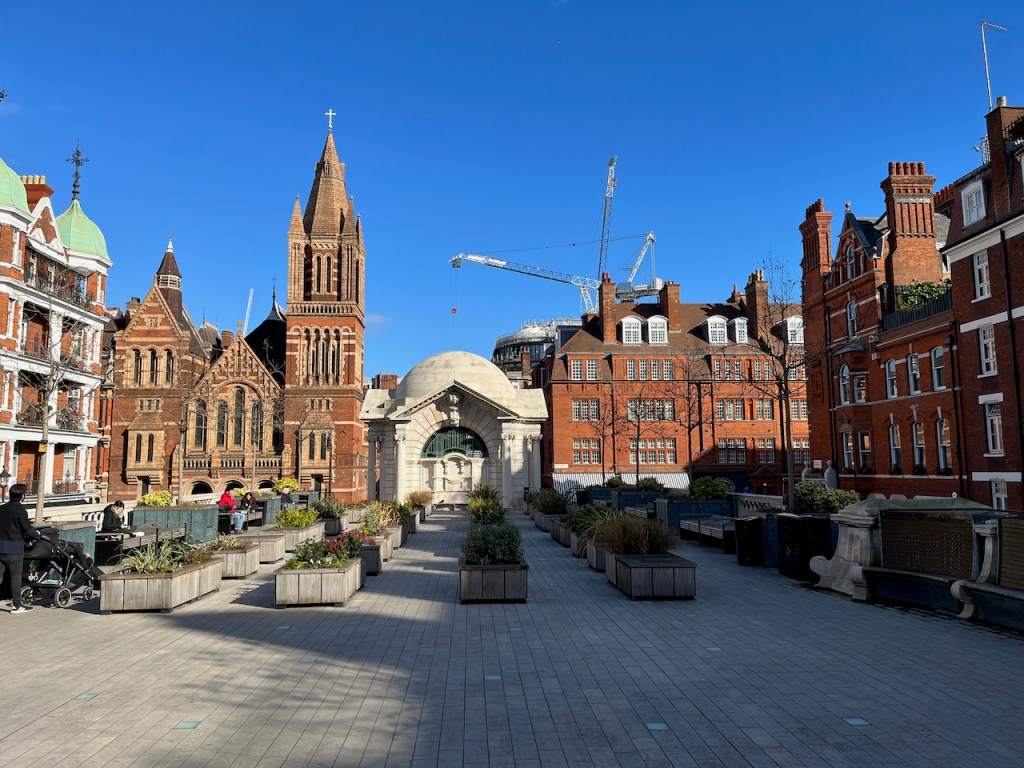 Brown Hart Gardens, a paved area with rows of square plant boxes in the centre, and benches along the sides. The garden is a raise area accessed by steps, so it's higher than the roads surrounding it.