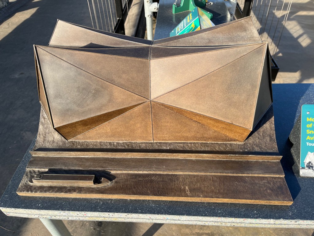 A tactile 3D model illustrating the shape of the aviary in Monkey Valley at London Zoo. On the front side of the structure, the roof slopes up in triangular sections to the left and right from a central point, peaking at each end of the building. The same occurs on the back half of the building.